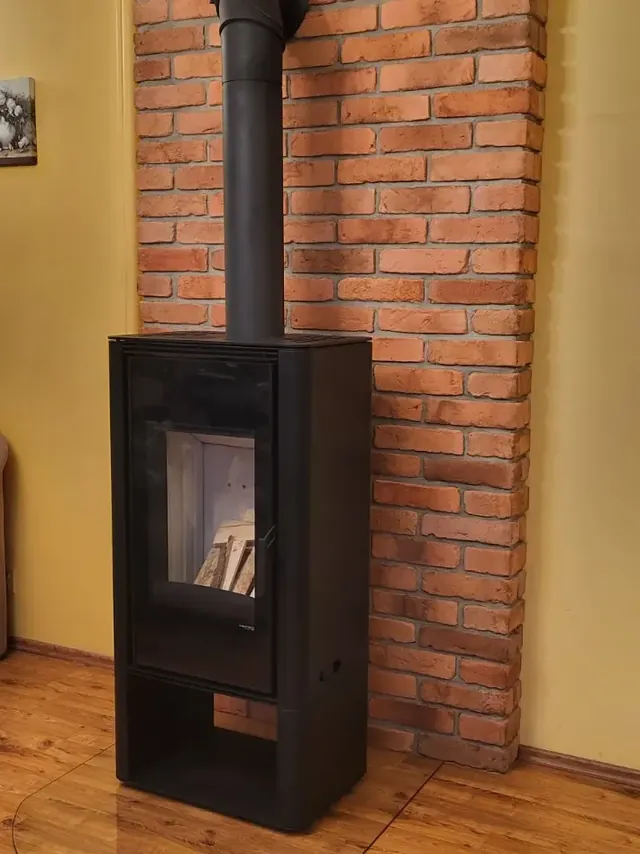 Czarny piec wolnostojący na tle ceglanej ściany — realizacja MAS Kominki